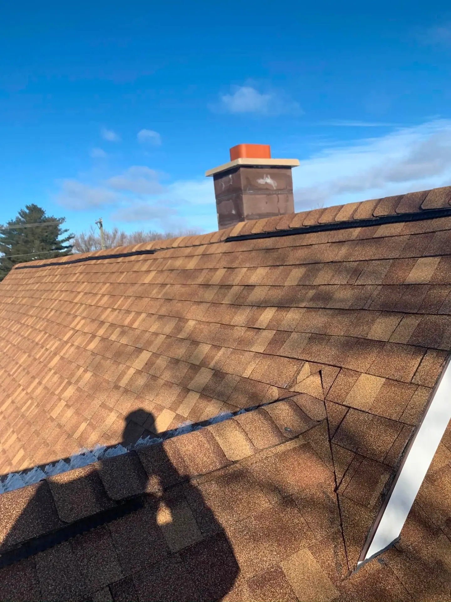 Completed shingle roof with chimney against a bright blue sky